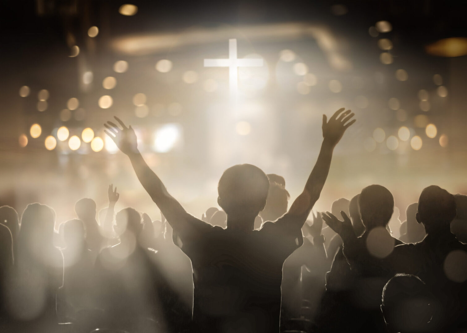 Person raising hands in worship with a glowing cross in the background.