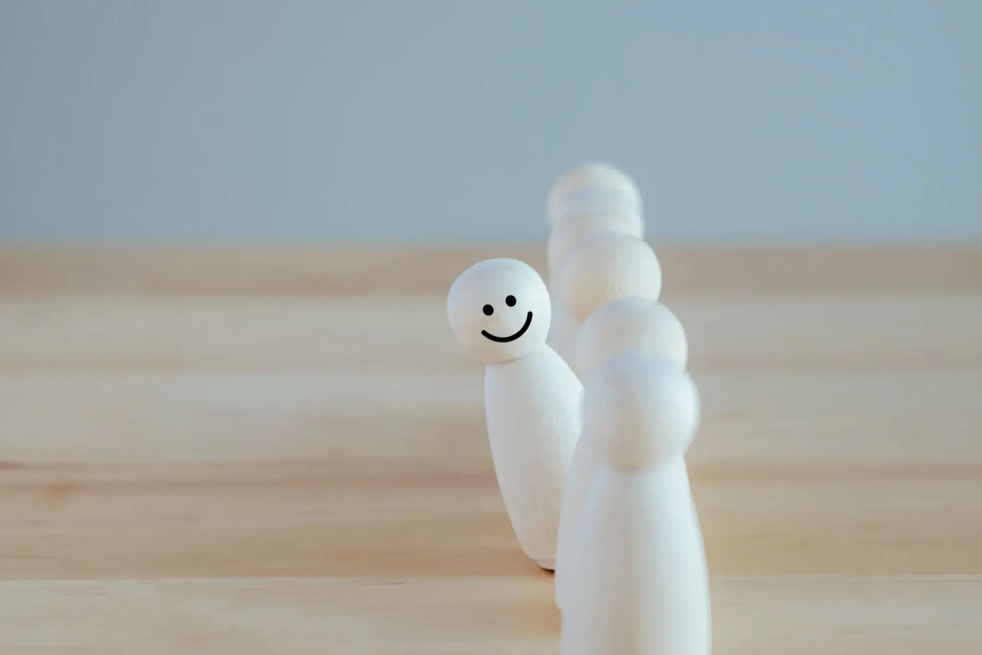 A smiling white bowling pin stands out among plain pins on a wooden surface.