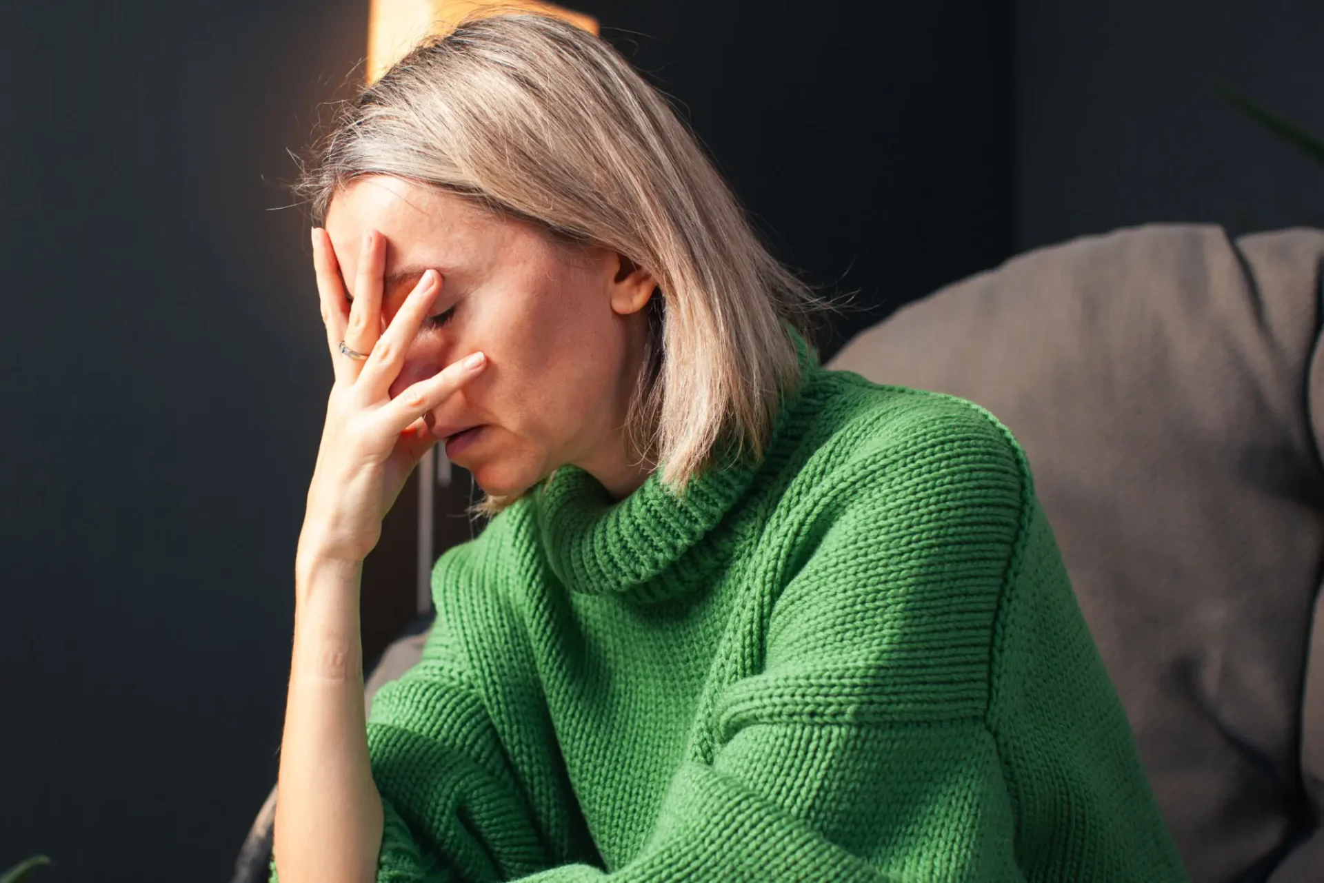 Woman in green sweater looking stressed and holding her face.